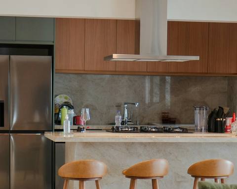 Open-plan kitchen with deep green tall cabinets, walnut uppers and a stone waterfall island